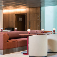Rust-colored upholstered sofa and cream circular chairs with red accent tables in a modern lounge setting.