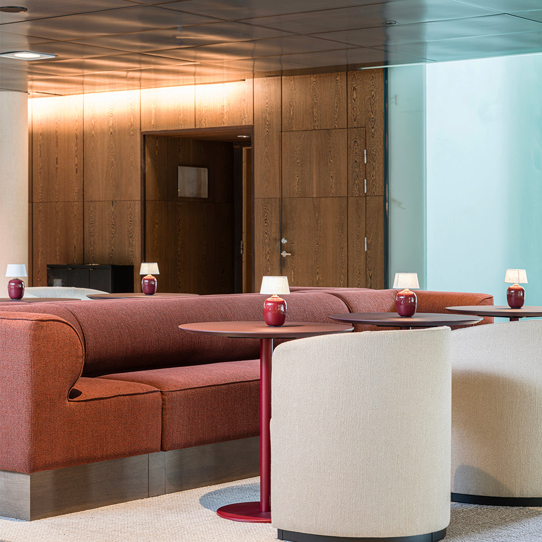 Modern lounge with rich rust orange and soft cream furniture, accented by deep red table bases and ambient lighting.
