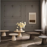 "Neutral toned tables in varied shapes and textures, set against a gray wall and bright floral centerpiece."