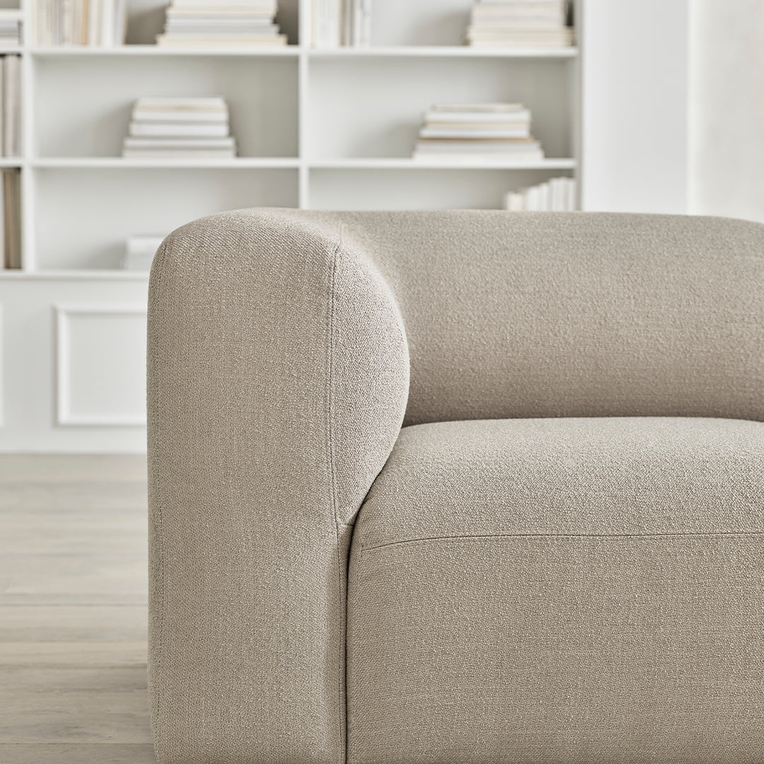 Beige upholstered sofa with smooth, rounded edges and subtle texture, set against a minimalist backdrop.