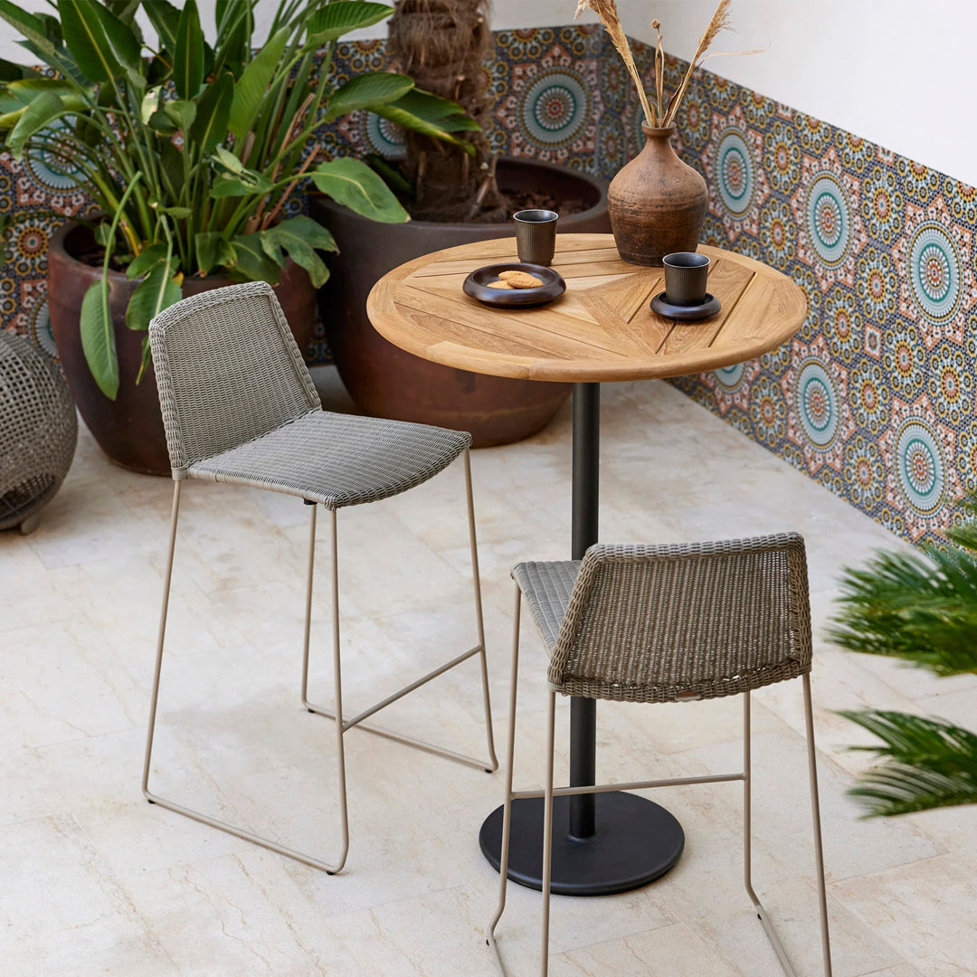 Gray woven chairs, wooden table, earthy pots, and colorful patterned wall enhance the vibrant outdoor seating area.