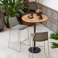 Gray woven chairs, wooden table, earthy pots, and colorful patterned wall enhance the vibrant outdoor seating area.