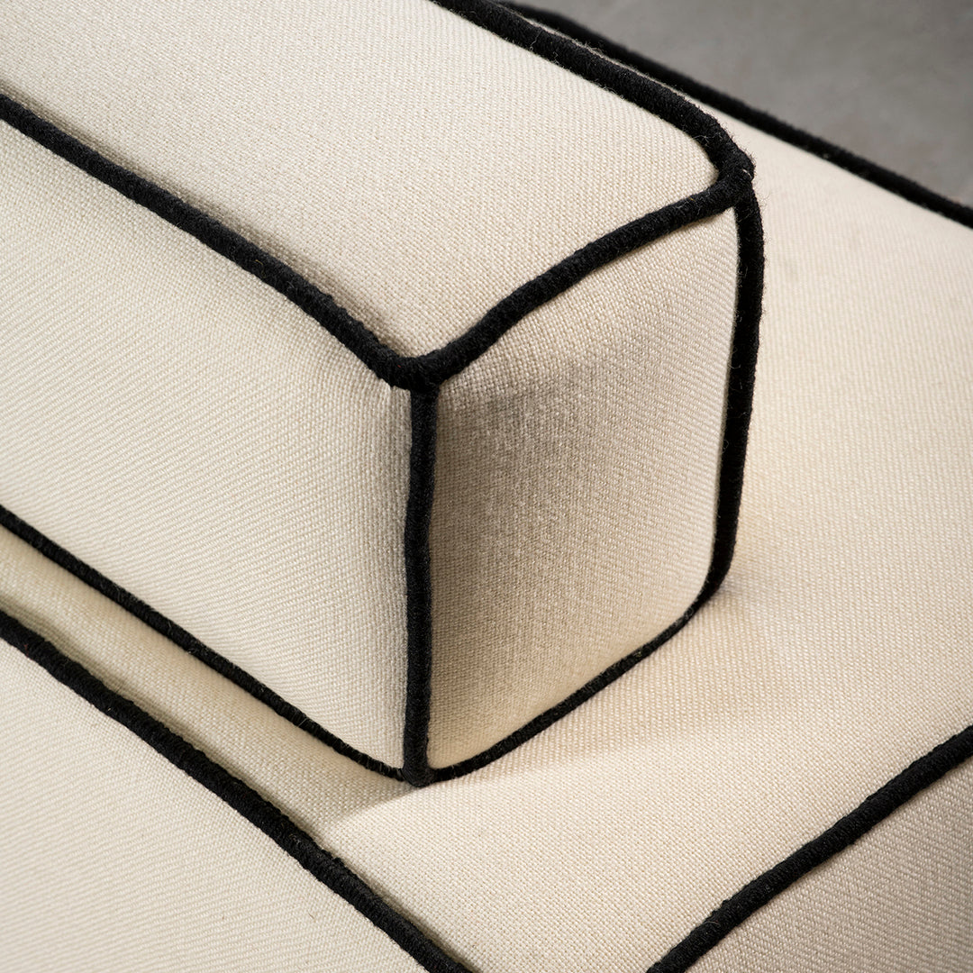 Beige fabric sofa cushion with contrasting black piping detail, showcasing a modern, clean design.