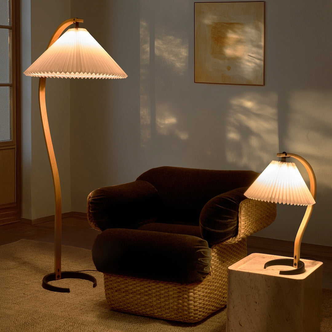 "Elegant cream pleated lampshades with warm wooden bases, set against a cozy dark brown sofa and neutral walls."