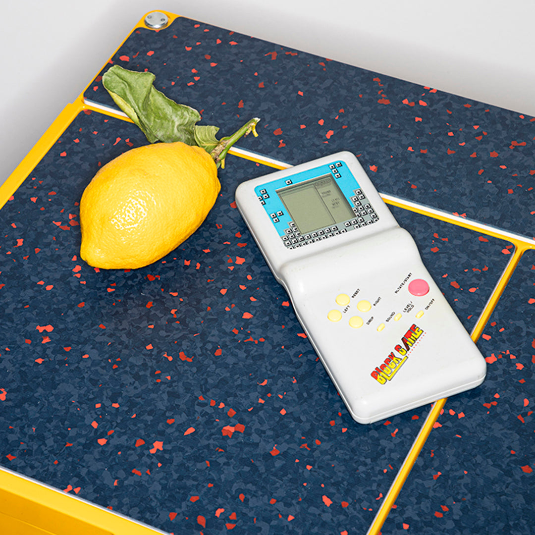 Yellow lemon on navy blue patterned surface with red specks and a white handheld game console nearby.
