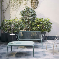 Mint green outdoor furniture set with a geometric patterned floor, surrounded by lush greenery.