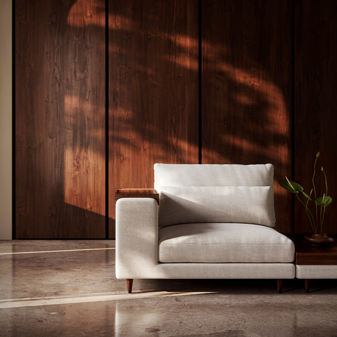 Modern white sofa with soft fabric and wooden armrest against a dark wooden panel background, featuring natural lighting.