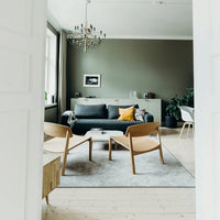 Modern living room with olive green walls, grey sofa, yellow accent pillow, and light wooden furniture.