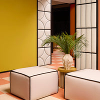 Modern room featuring vibrant yellow, soft pink, geometric white patterns, and lush green foliage in a stylish setting.