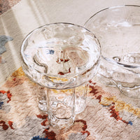 Clear glass stool with a textured surface on a multicolored patterned rug featuring shades of red, orange, blue, and cream.