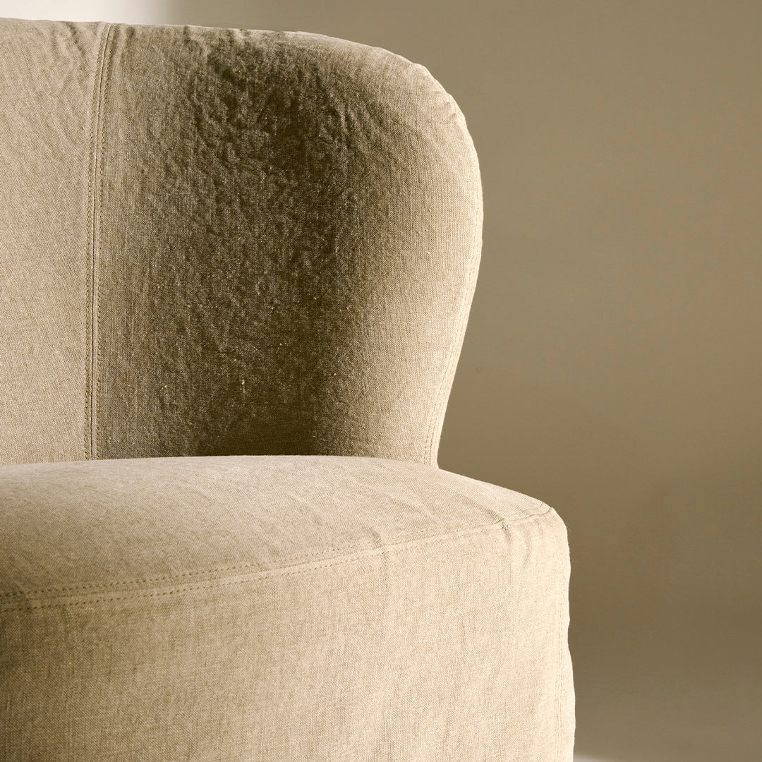 Beige upholstered armchair with a soft, textured fabric and curved design against a neutral background.