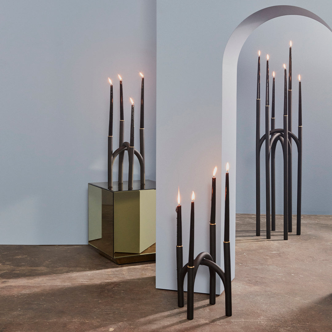 Black candlesticks with gold accents on a soft blue backdrop and reflective surfaces, creating a modern and elegant aesthetic.