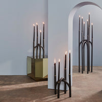 Black candlesticks with gold accents on a soft blue backdrop and reflective surfaces, creating a modern and elegant aesthetic.