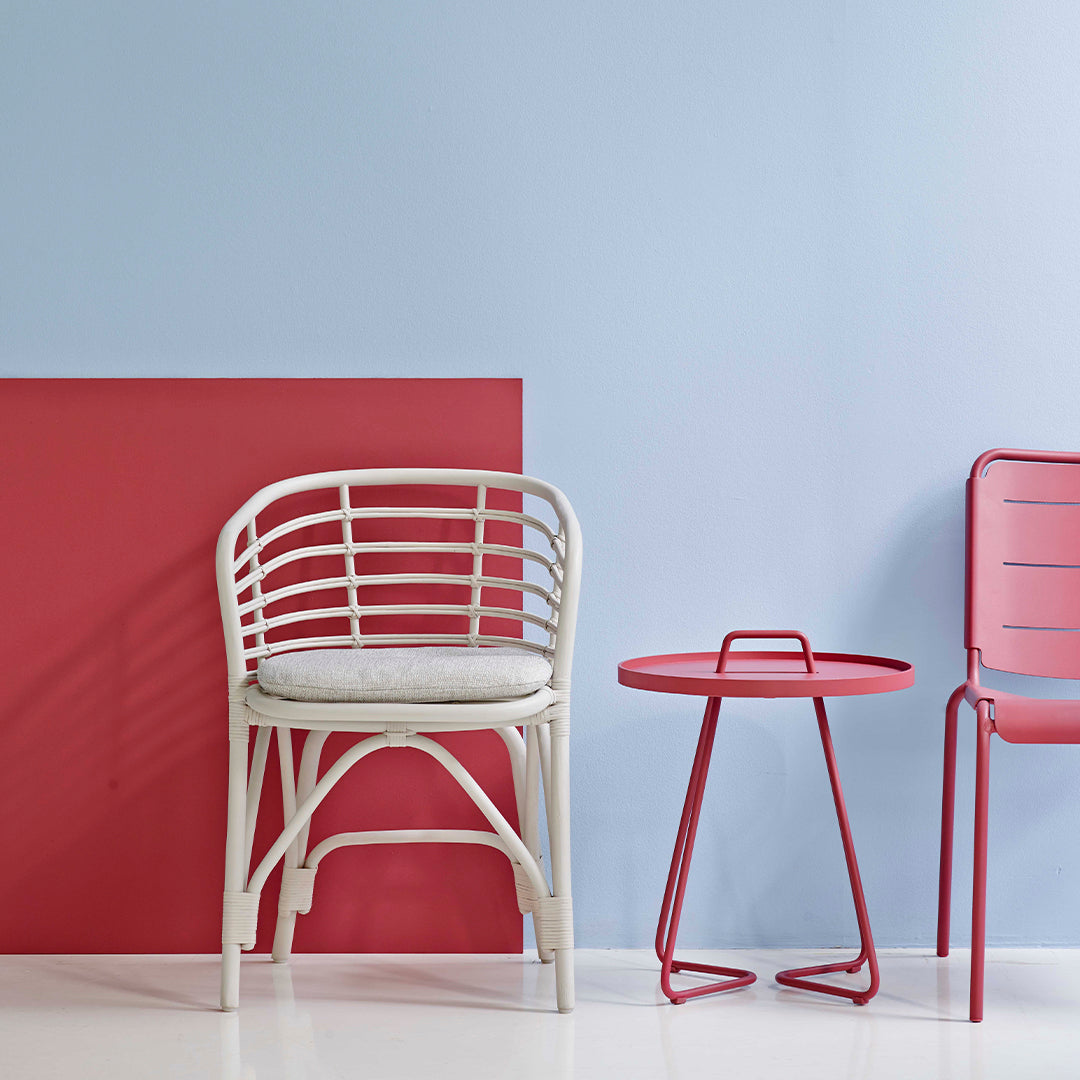 "White and red striped chair with pink side table against a light blue and red geometric background."