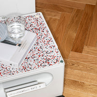 White side table with a colorful speckled red, black, and white top on a wooden floor.