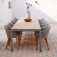 Outdoor dining set featuring gray upholstered chairs and a natural wood table, complemented by a neutral stone backdrop.