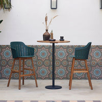 Stylish green chairs and wooden table with vibrant, patterned tile backdrop in earth tones and teal accents.