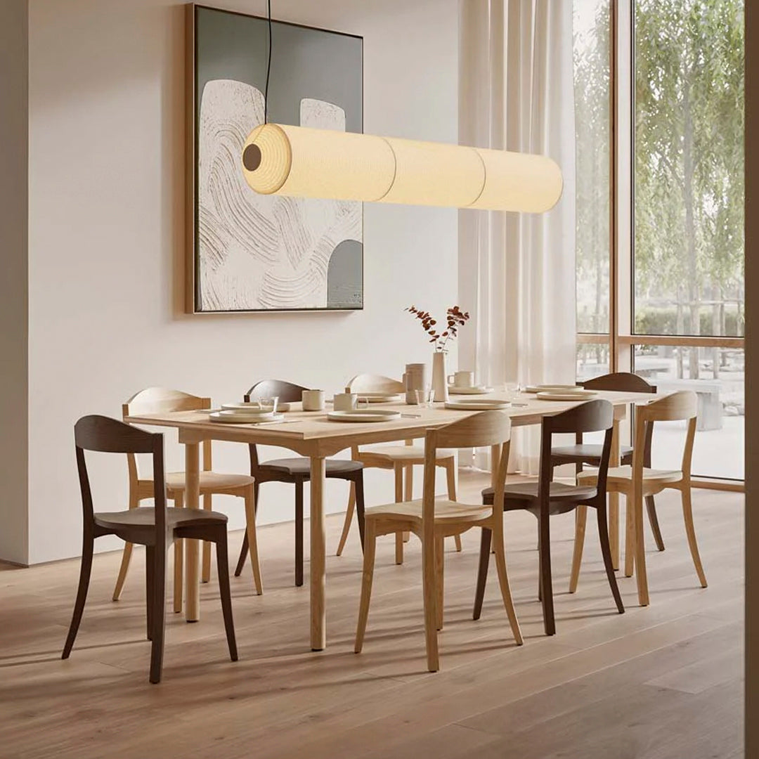 Light wood dining table with natural wooden chairs and soft beige pendant lighting against a neutral-toned backdrop.