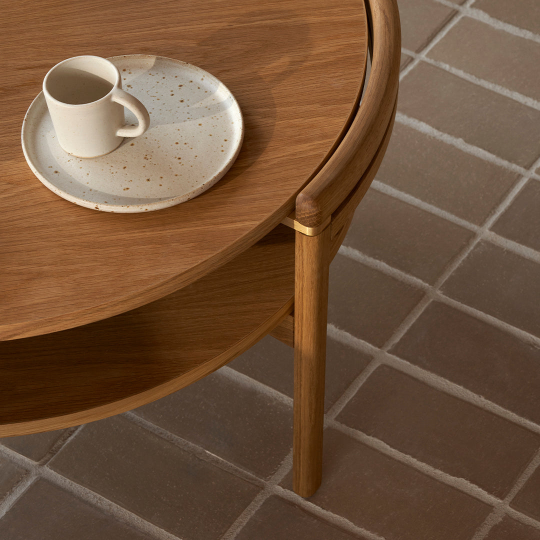 Wooden coffee table with rounded edges, featuring a beige speckled plate and cup on a light brown tiled floor.