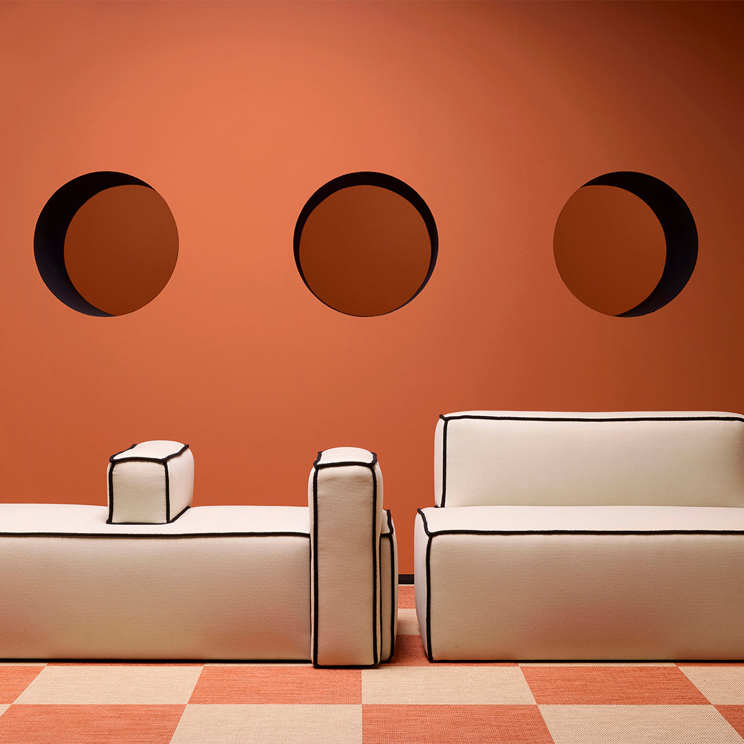 White sofas with black trim against an orange wall with circular cutouts, featuring a patterned orange and cream floor.