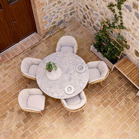 Stylish round marble dining table with light beige cushioned chairs, set against rustic stone and terracotta flooring.