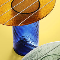 Colorful glass tabletop with a vibrant orange top, blue base, and smooth green accents on a yellow background.
