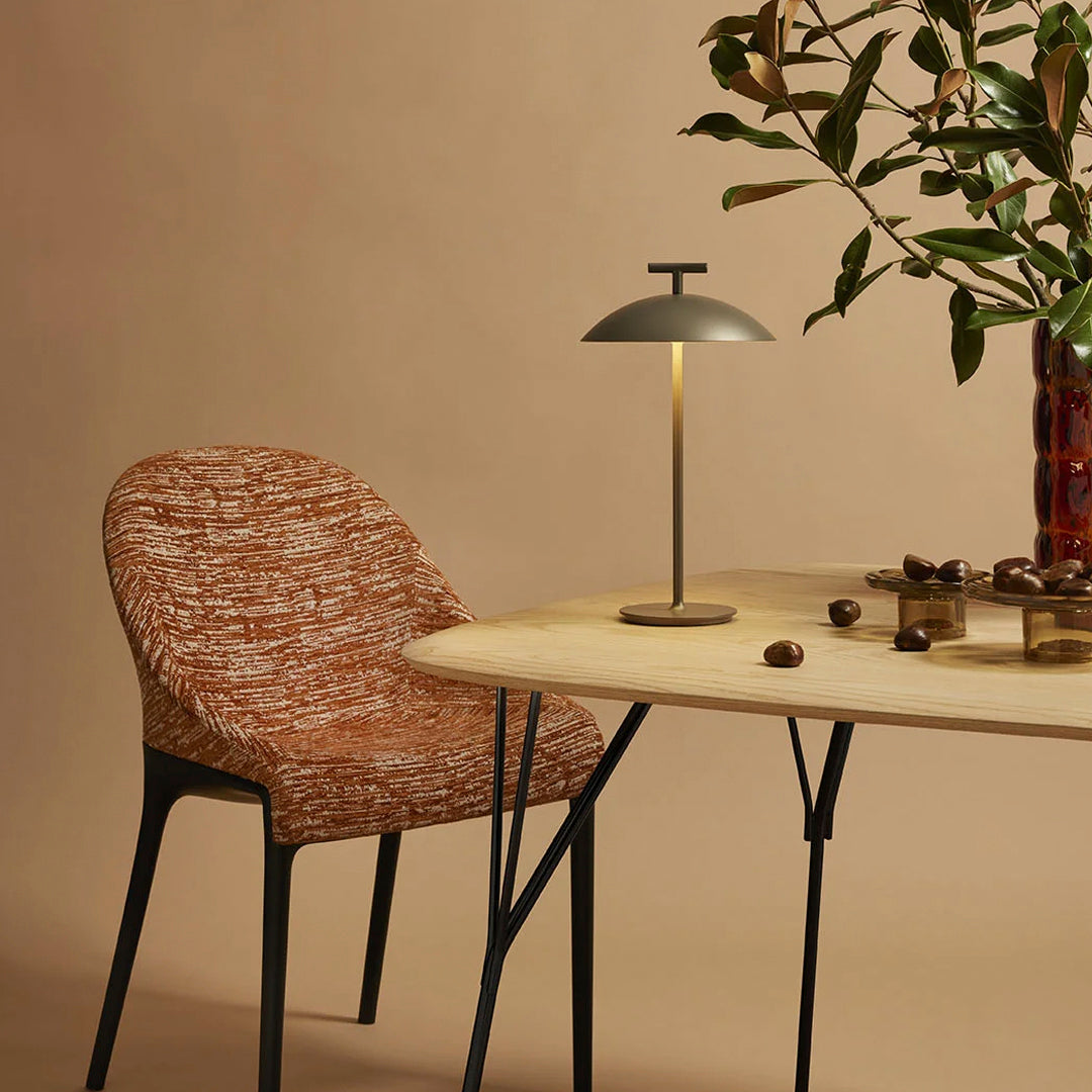 Rust-colored patterned chair beside a sleek, modern lamp on a light wood table against a soft beige background.