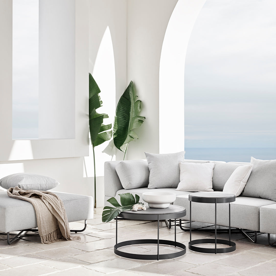 Modern gray sectional sofa with soft cushions, paired with sleek black tables and light, airy decor.