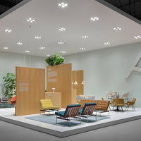 Modern exhibition space featuring warm wooden panels, colorful upholstered chairs in yellow, blue, and orange hues.