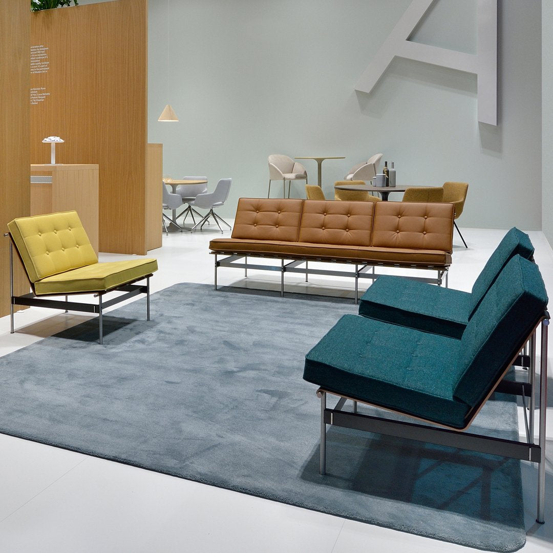 Modern seating arrangement featuring yellow, brown, and teal upholstery on sleek metal frames, with a gray rug.