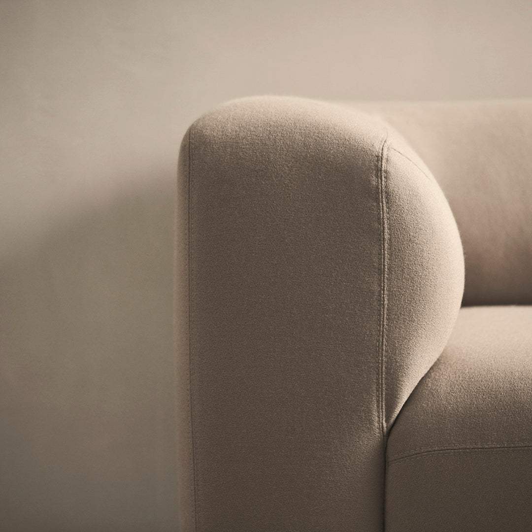 Beige upholstered sofa corner with smooth curves and soft texture, showcasing minimalist design and neutral tones.