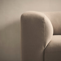 Beige upholstered sofa corner with smooth curves and soft texture, showcasing minimalist design and neutral tones.