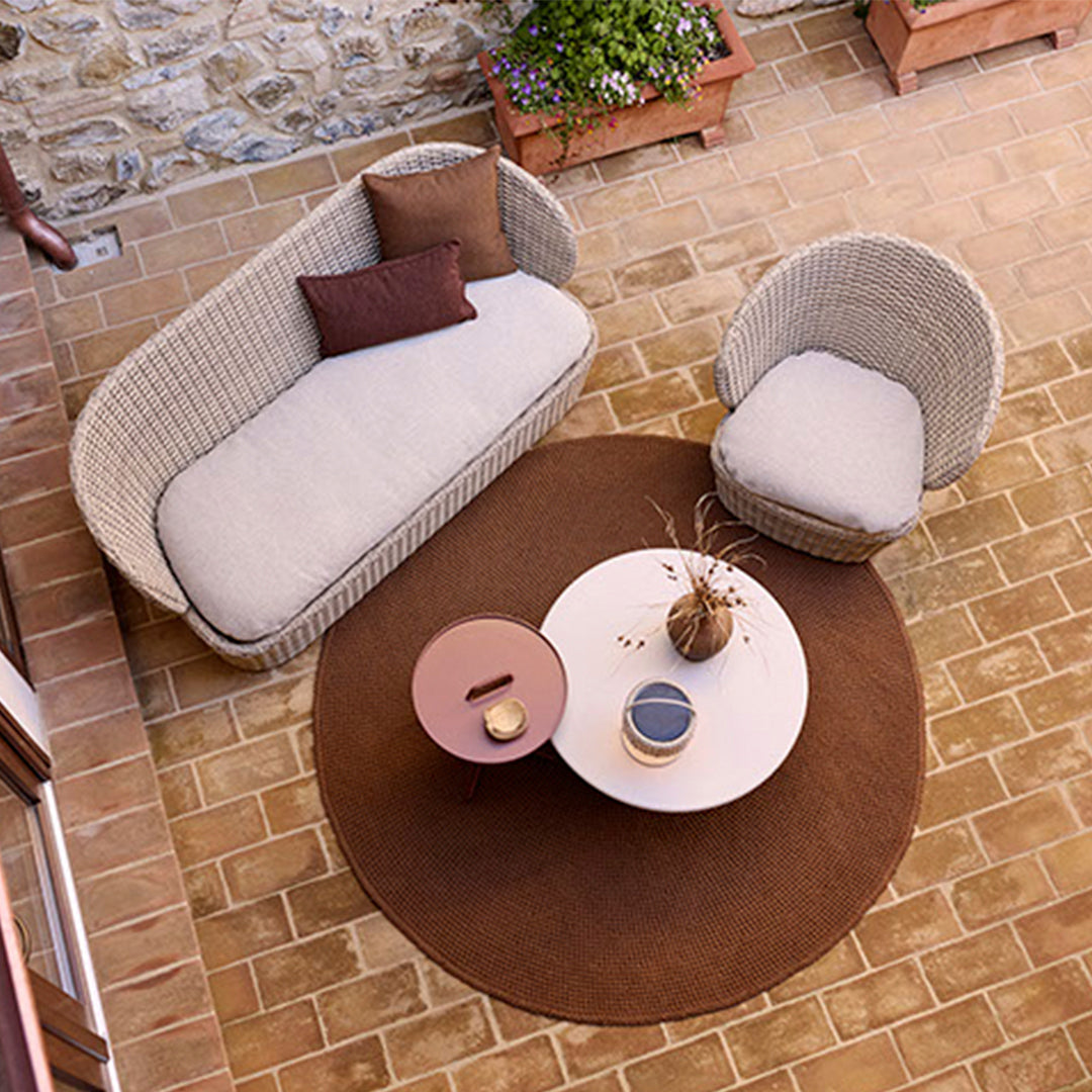 Outdoor seating with neutral beige cushions, brown circular rug, and a round white table in a natural stone setting.