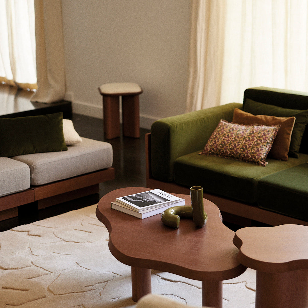 Green and beige sofas with patterned accent pillows on a wooden coffee table and textured cream rug.
