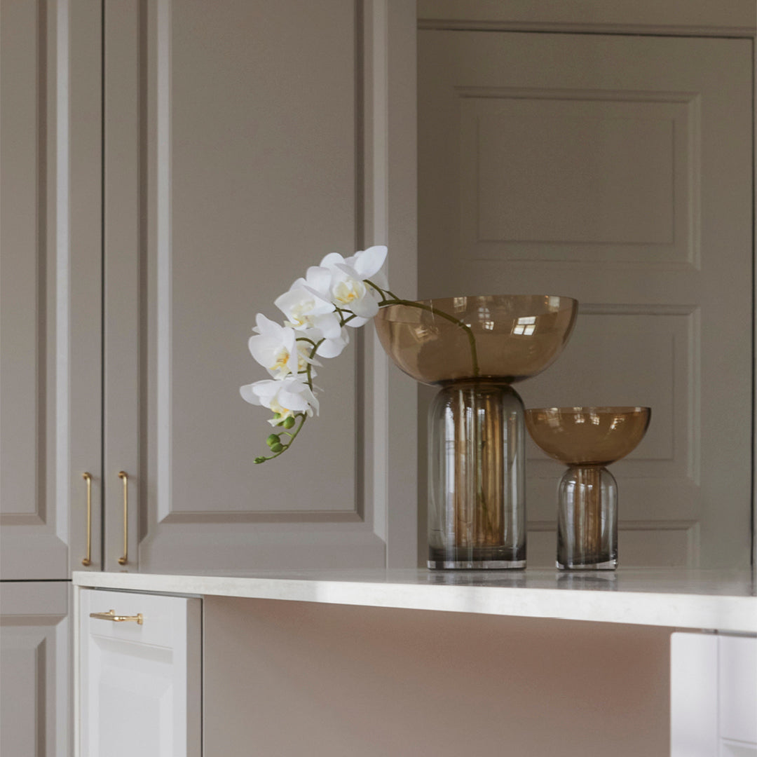 Elegant glass vases in earthy brown tones with a smooth finish, complemented by a white orchid bloom.