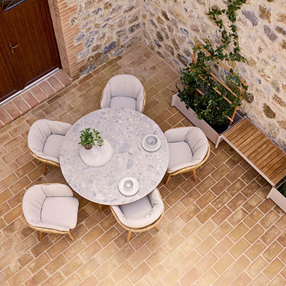 Round stone dining table with soft beige chairs, set against a rustic stone wall and warm terracotta tiles.