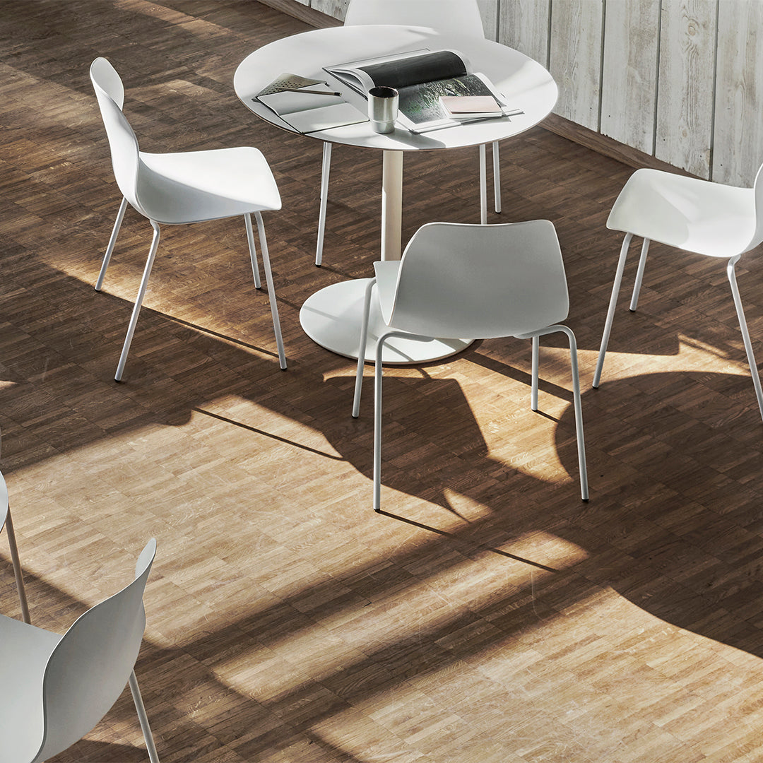 White chairs and round table set against a warm, brown wooden floor, featuring sleek, modern lines.