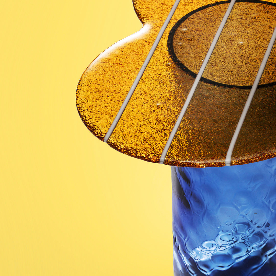 Amber guitar-shaped decor on a blue base against a bright yellow background, showcasing vibrant colors and elegant patterns.