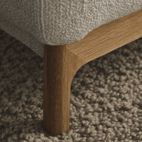 Light gray upholstered furniture leg with a natural wood finish over a textured beige rug.