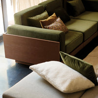 Green upholstered sofa with patterned and solid pillows in earthy tones, complemented by a wooden base and neutral cushions.