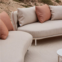 Beige curved outdoor sofa with terracotta cushions, featuring a textured surface design. Stylish and modern patterns.