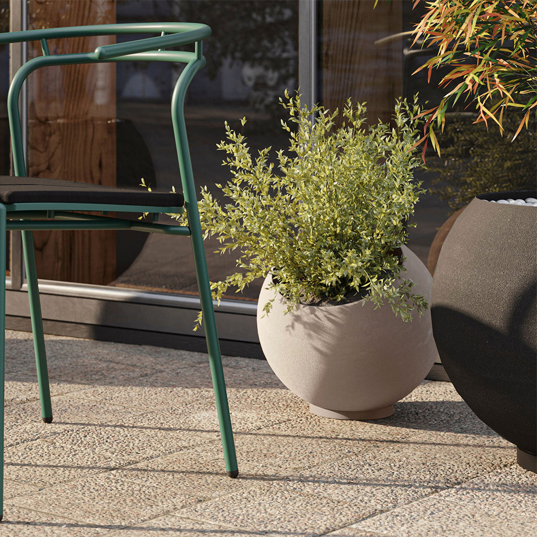 Green metal chair with black cushion, light grey round pot, and dark textured planter on a stone patio.