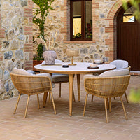 "Round white table with beige and light gray woven chairs in a rustic stone setting."
