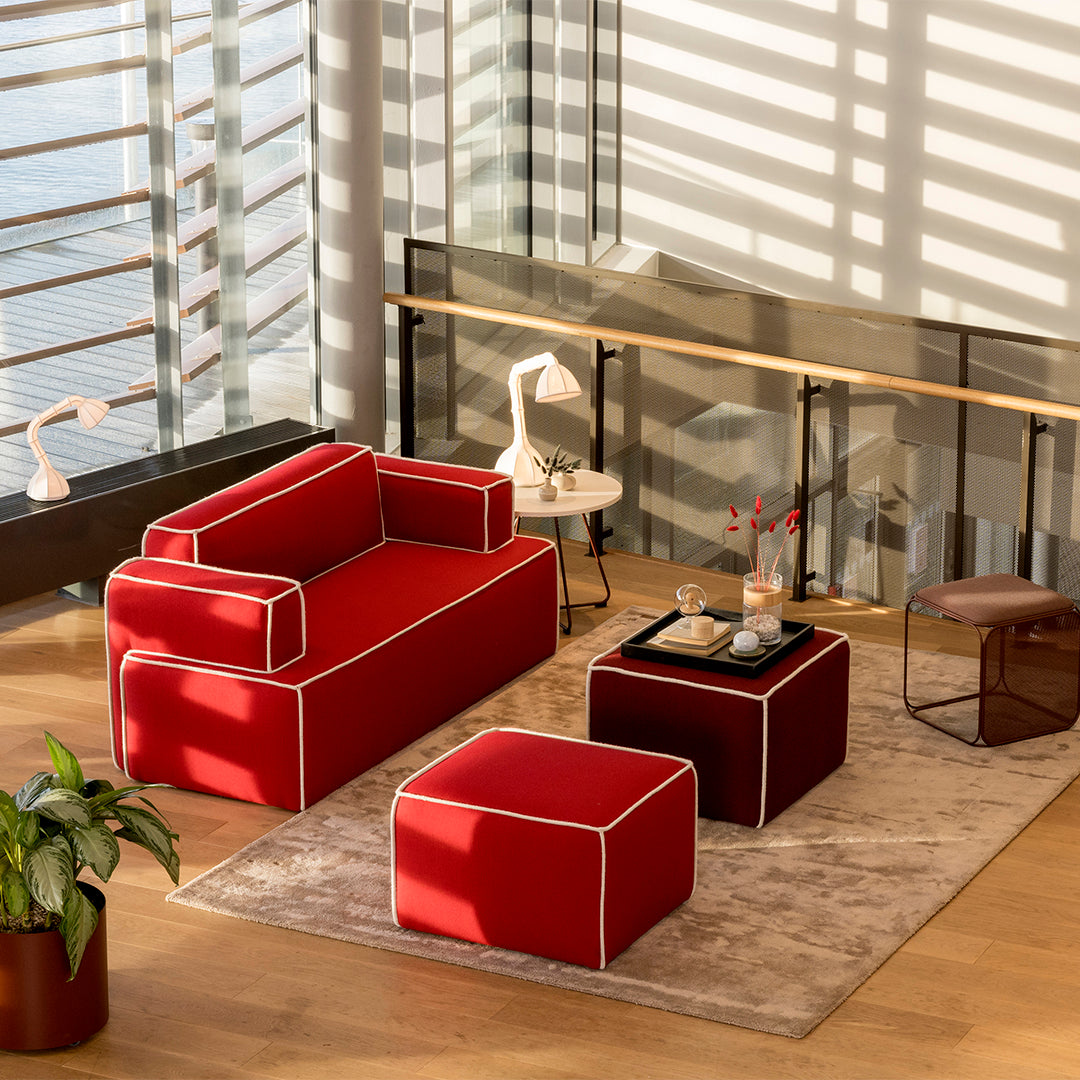 Red sofa and ottoman with white piping, paired with a dark accent table on a soft beige rug in a modern setting.