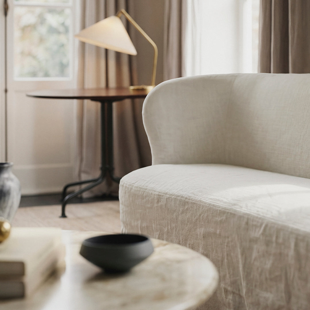 Light beige curved sofa with subtle texture, paired with a black bowl and neutral furnishings in a cozy living space.