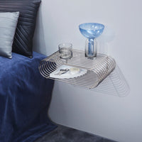 Silver metal wall shelf with blue glass vase, gray pillow, and navy blue bedding. Modern, sleek design with soft tones.