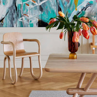Wooden chair and table in muted tones, with vibrant orange tulips and a bold turquoise abstract wall art background.
