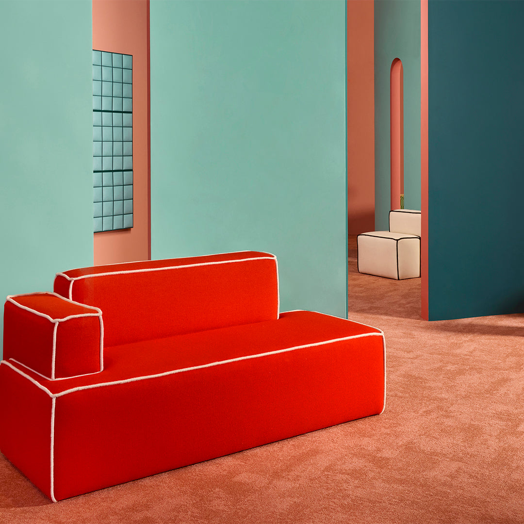 Modern red sofa with white piping against teal and peach walls, featuring soft brown carpet and minimalist decor.