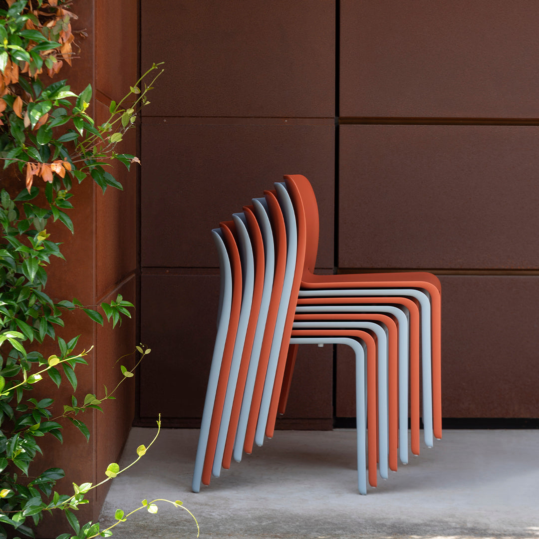 Stacked chairs featuring a warm terracotta hue with sleek gray legs against a rich brown background.