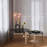 Stylish black marble coffee tables with natural wood legs, featuring sleek black and copper candle holders and a green vase.